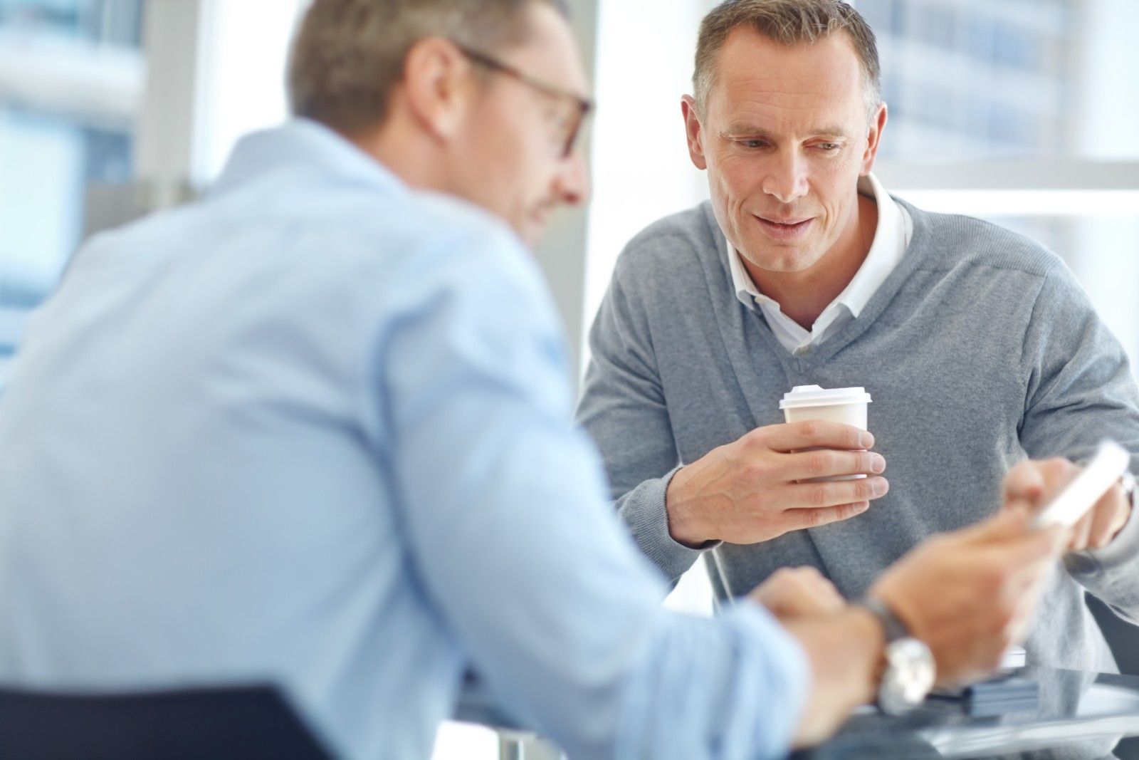 Zwei Männer unterhalten sich bei einer Tasse Kaffee entspannt über ein Business-Thema.